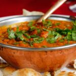 Delicious Indian curry garnished with cilantro served with naan in a copper dish.