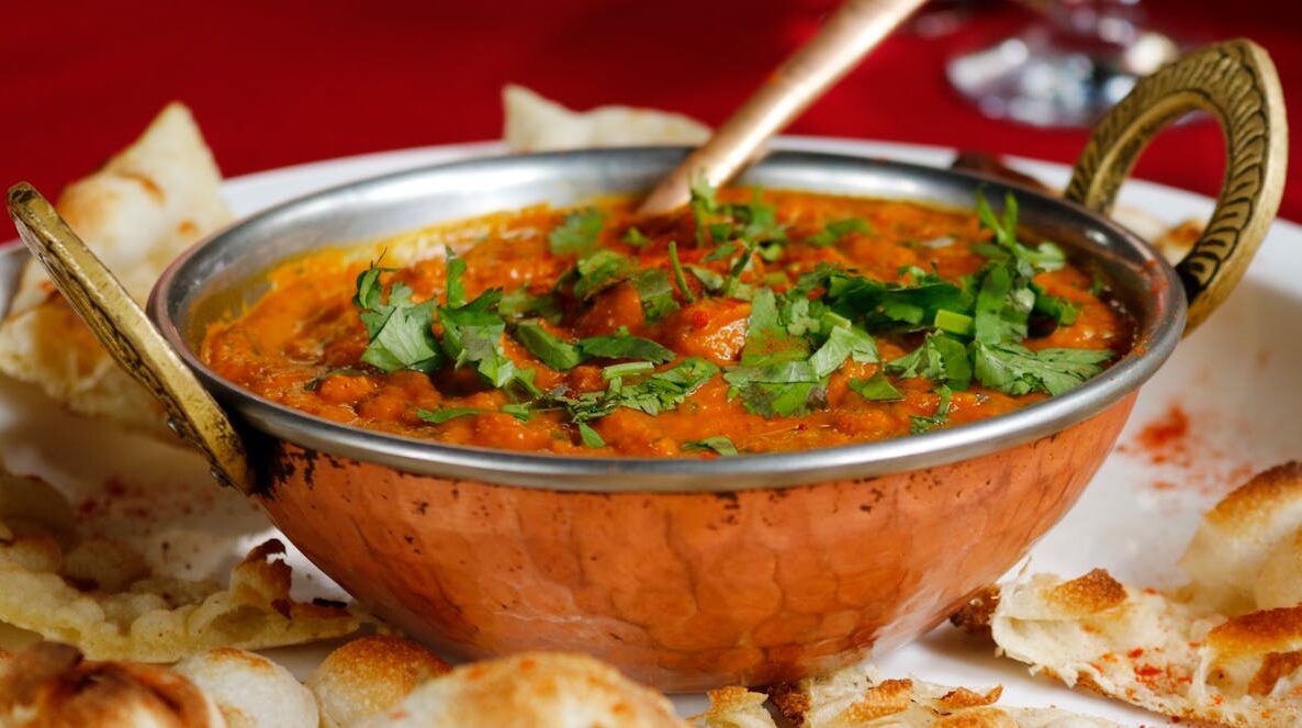 Delicious Indian curry garnished with cilantro served with naan in a copper dish.