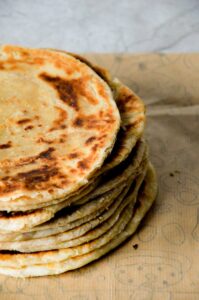 A stack of freshly baked homemade flatbread on rustic paper, showcasing a golden crispy texture.